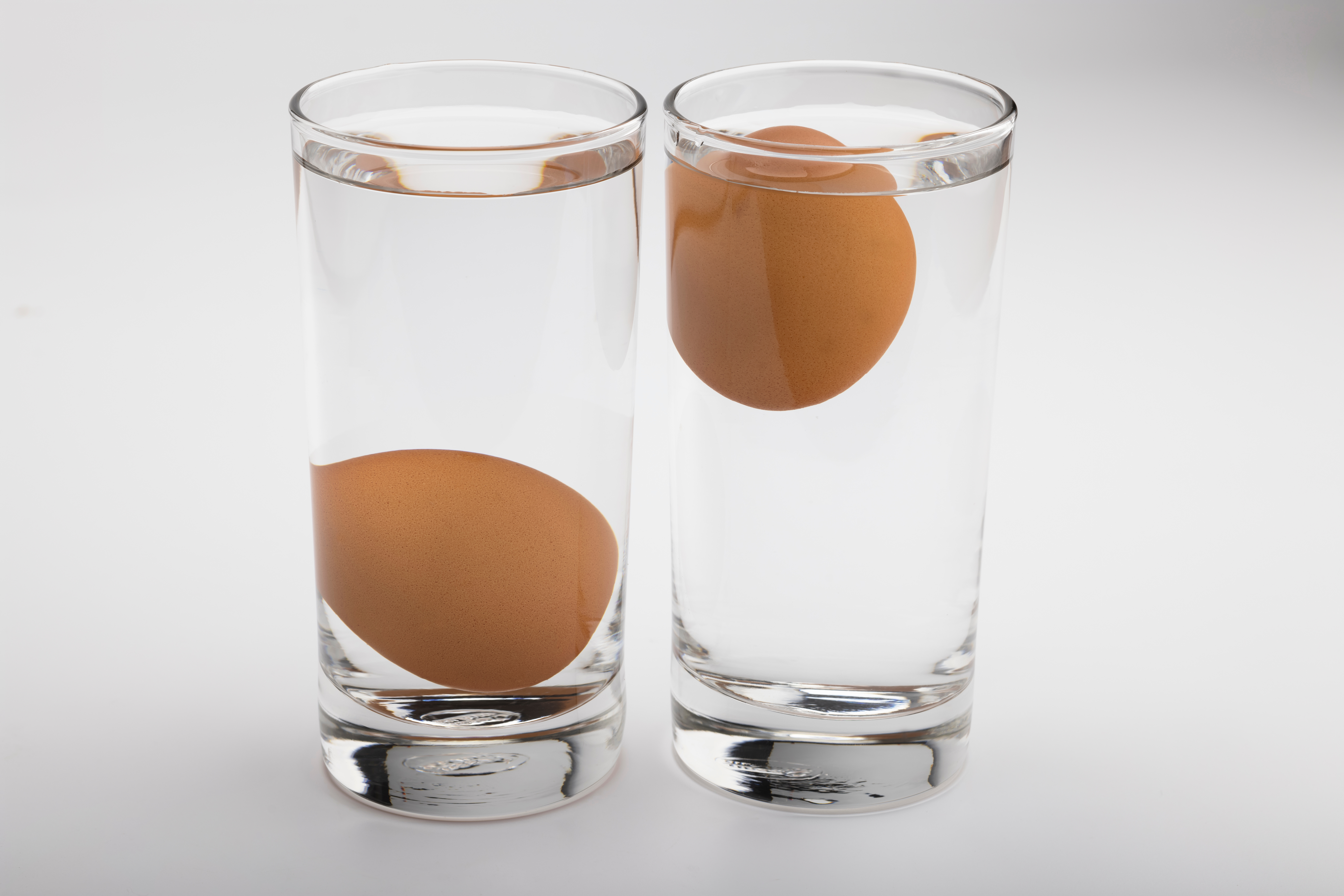 Zwei mit Wasser gefüllte Gläser. In einem liegt das Ei auf dem Boden des Glases, im anderen schwimmt es an der Oberfläche.